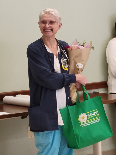 Daisy Award winner nurse Barbara Powers holding flowers and tote bag 